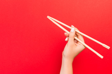 Woman's hand holding chopsticks on red background. Chinese food concept with empty space for your...
