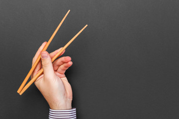 Creative image of wooden chopsticks in male hands on black background. Japanese and chinese food...