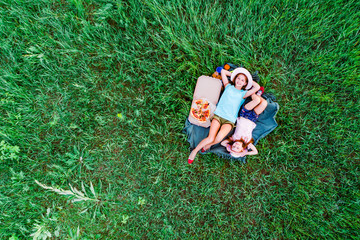 two little girls have a picnic with pizza and lying on a green grass, aerial top view