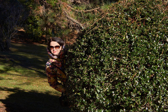 Young Woman Standing Behind Topiary At Park