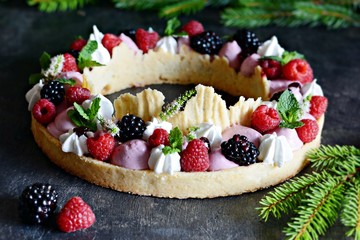 Tasty tart with air cream, berry jam, fresh berries, meringue and mint on a dark background. Delicious pie with ripe wild berry.  Gourmet french dessert.