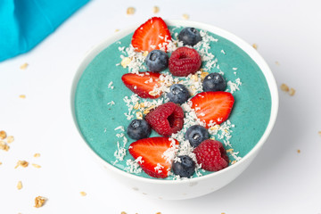 Blue spirulina smoothie bowl topped with blueberries, strawberries, raspberries and coconut.