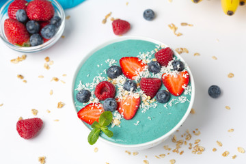 Blue spirulina smoothie bowl topped with blueberries, strawberries, raspberries and coconut.