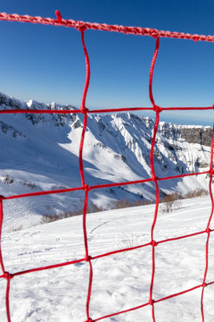 Red prohibition grid, ski resort stuff, symbol of dangerous, closed ski piste, closed slope, forbidden to go or ride, beautiful snowy mountain panorama with clear blue ski background. Vertical image
