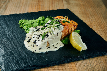 Serving of grilled salmon steak in cream-cheese sauce and mashed green peas garnished. Close up, selective focus