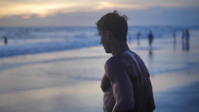 Portrait of young man, the well-trained muscular athlete, posing on the beach at sunset