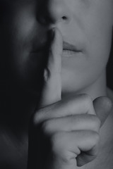 Conceptual monochrome image of woman holding finger to her lips keep quiet - 329874950