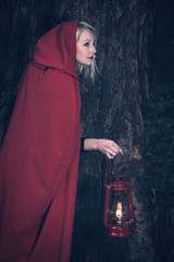 Attractive woman dressed a little red riding-hood walk in a dark forest with lantern - 329875173
