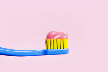 Bright toothbrush with pink paste close-up on a pink background.