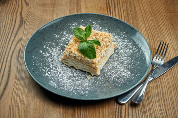 Close up view on piece of cake Napoleon with strawberry on ceramic plate on wooden background. Russian cuisine, multi layered cake with pastry cream. Selective focus
