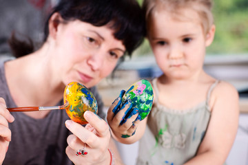 Mum and daughter decorate and paint easter eggs with brush in multi color. Tradition and fun before Easter holidays. Close up and face.