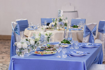 Blue and white flowers in glass vases are on the table in the restaurant on the wedding day. Festive table setting