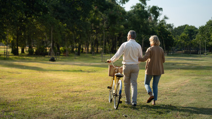 The behind of Caucasian elderly couples walking with a bicycle in the natural autumn sunlight...