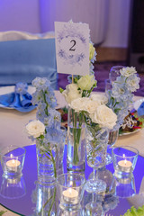 Blue and white flowers in glass vases are on the table in the restaurant on the wedding day. table number two