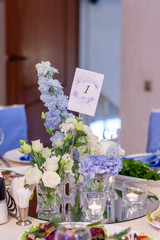 Blue and white flowers in glass vases are on the table in the restaurant on the wedding day. table number one