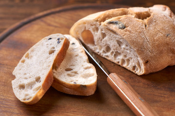 Ciabatta with olives, sliced. Fresh diet homemade bread baked according to a traditional Italian recipe. Rustic table, wooden cutting board. Knife for bread.