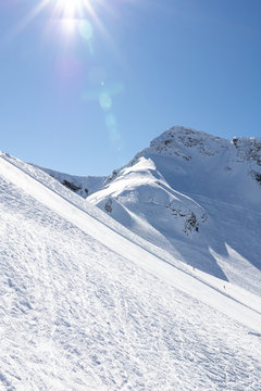 Ski resort panorama, view on ski slope and great snowy mountains in sunny day, blue sky backwards. Vertical picture with back light. Actual lifestyle, hobby and vacation.