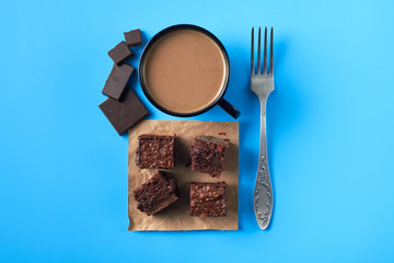 Flatlay with brownie pieces with coffeee cup,chocolate and silver fork on a blue table.