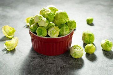Fresh raw Brussels sprouts in ceramic bowl on dark stone background. Healthy food concept.