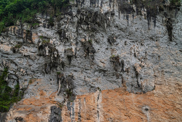 Guilin, China - May 10, 2010: Along Li River. Closeup of gray-brown-black wall of cliff of karst mountain vertically in green water. Stalactites partly covered by moss.