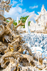 The white temple (Wat Rong Khun) in Chiang Rai city, Thailand. Beautiful buddhist ancient building with bridge above damned souls of sinners, path to the heaven. Famous tourist destination. Blue sky