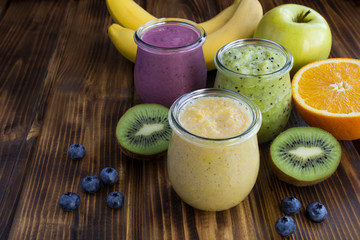 Different fruit smoothies or puree in the small glass jars on the brown wooden  background. Closeup.