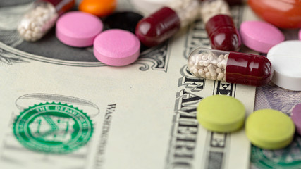 The concept of making money on medicines. Multicolored drugs on a background of dollars. Different remedy, pills, capsule, antibiotic and vitamin.