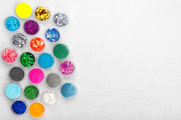 Obraz na płótnie Canvas Creative flat lay overhead composition with sequins, glitter, mica and shimmer for nail design in plastic jars on a light wooden background. Top view. Free copy space