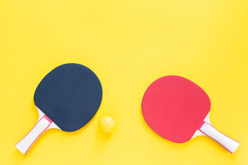 Red and black tennis ping pong rackets and orange ball isolated on a yellow background, sport equipment for table tennis