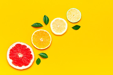 Flat lay composition with slices of fresh lemon orange grapefruit lime green leaves on yellow background top view copy space. Citrus Juice Concept, Vitamin C, Fruits. Creative summer background