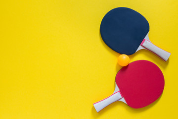 Red and black tennis ping pong rackets and orange ball isolated on a yellow background, sport equipment for table tennis