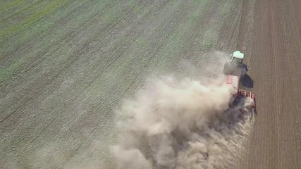 Top down aerial view of green tractor cultivating ground and seeding a dry field. Farmer preparing land with seedbed cultivator as part of pre seeding activities in early spring season of agricultural
