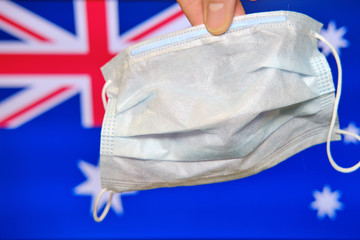 A hand holds a mask against the background of the flag of Australia. Fighting coronavirus in an Australian city