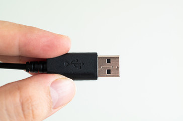 USB cable connector plug close up shot held between fingers by Caucasian male hand isolated against white
