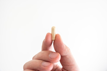 Nondescript medical pill held between fingers by Caucasian male hands close up shot isolated on white