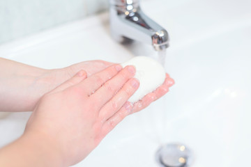 Washing hands for health care. Cleaning hands with soap cube and stream of water in bathroom. White...