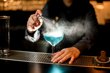 bartender sprinkles on blue cocktail in glass on bar