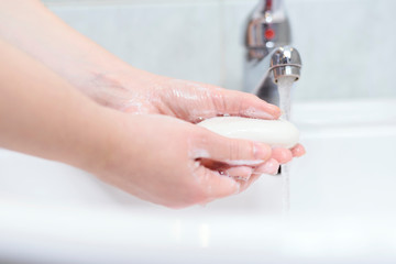 Washing hands for health care. Cleaning hands with soap and strem of water in bathroom. White sink with silver faucet.