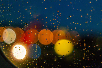 Circular round blur bokeh lights behind window with water droplets at night