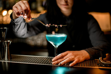Barman accurately hold tweezer with flower over cocktail glass.