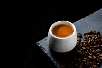 Fresh hot brewed espresso in white cup on black plate with roasted coffee beans