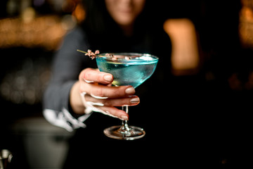 woman bartender holds blue cocktail on outstretched hand