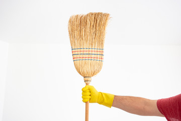 White Caucasian male hand with yellow latex glove holding a broom isolated against white background