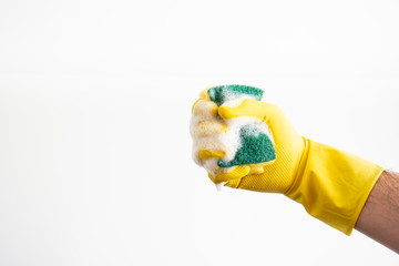 White Caucasian male hand with yellow latex glove holding a wet and soapy cleaning sponge against white background