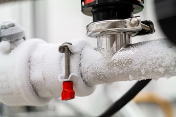 Frozen liquid nitrogen carrying pipes with a valve and black plastic lever close up in a science...