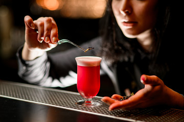 Bartender accurately hold tweezer with flower over cocktail glass.