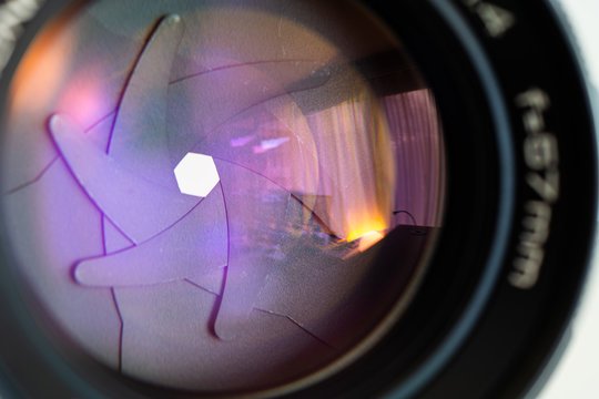 Old vintage fast aperture prime lens front element close up show colorful coating reflections and visible aperture blades