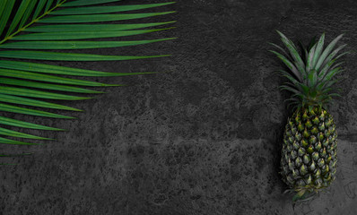green tropical palm leaves and pineapple mockup on natural black stone background with copyspace top view.
