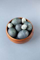 Creatively painted chicken and quail Easter eggs with natural hibiscus dye, look like sea stones in bowl on gray background, copy space. Happy Easter DIY concept. Soft selective focus. Flat lay