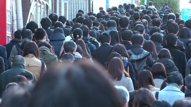 TOKYO, JAPAN - MARCH 2020 : View of crowd of people walking down the street in busy morning rush hour. Many commuters going to work. Japanese business man and woman, job and lifestyle concept.